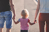 Back view of a man and a woman holding a childs hands between them