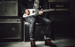 Guitar being played by person sitting on a guitar amplifier