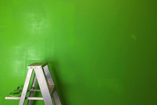 Step ladder with paint can in front of green wall