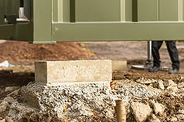 Close up view of corner of container home unit being lowered on to concrete support