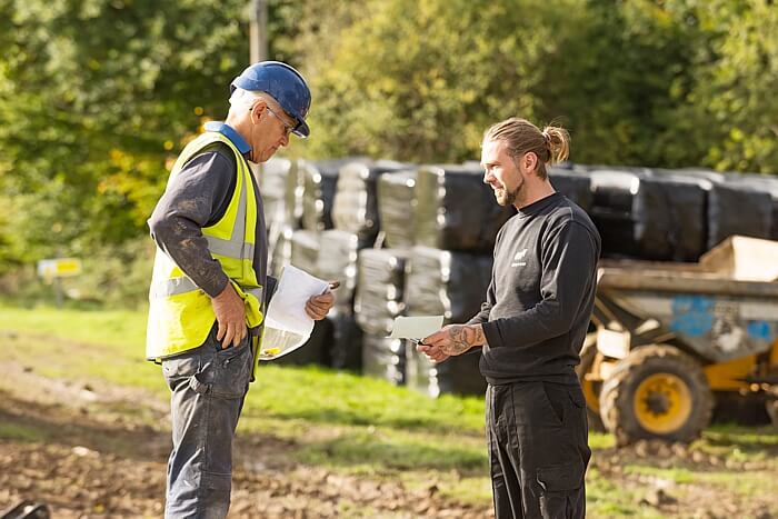 Two men in a field. One in a hi vis jacket