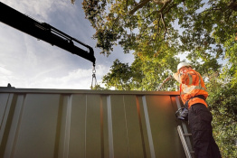 Man in hi vis jacket on ladder wearing hi vis jacket with container home being moved by a crane