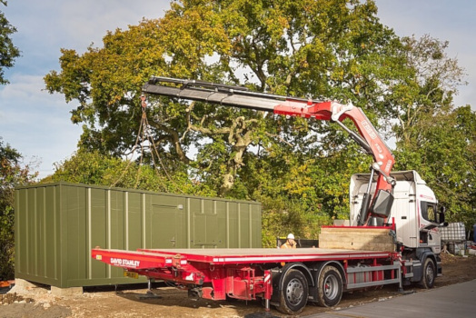 Flat bed truck crane beside container housing unit