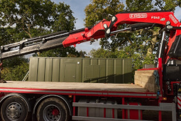 Lorry with crane attachment in front of a container housing unit